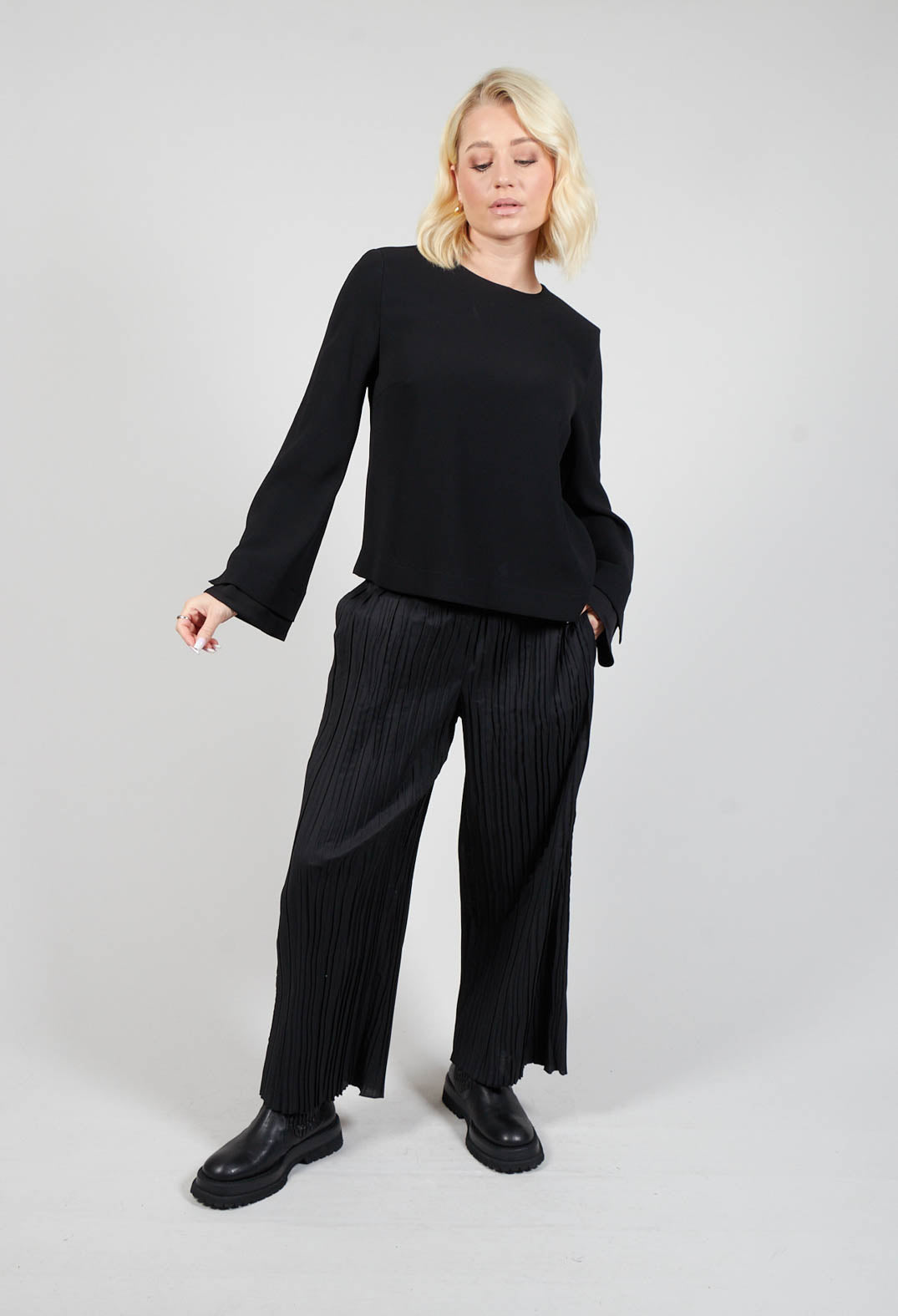 lady wearing a long sleeve leo blouse in black with pleated trousers and chunky boots