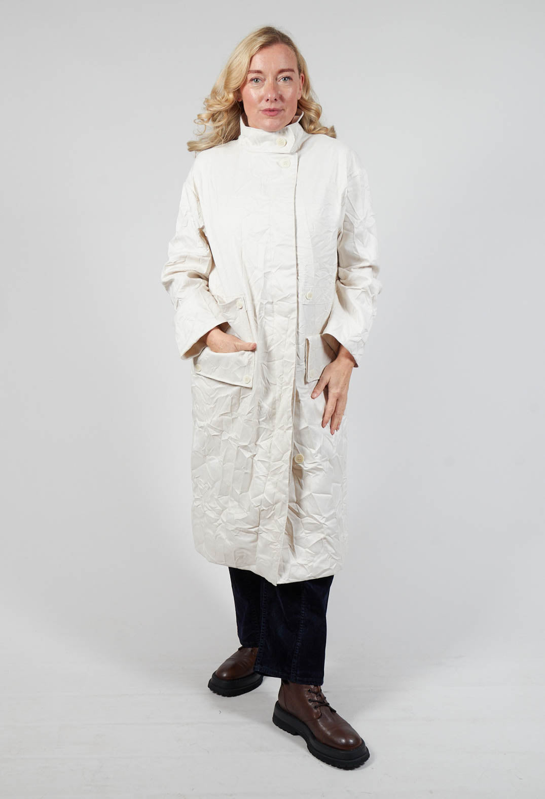 lady smiling wearing a long perry coat in off white shade with side pockets